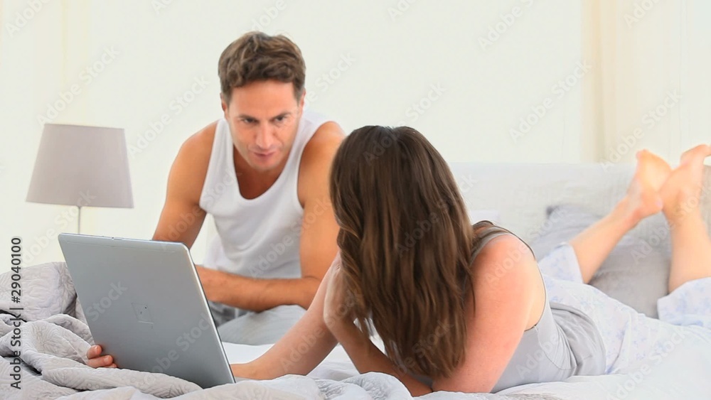 Pretty woman on her laptop while her husband is reading Pretty woman on her laptop while her husband is reading
