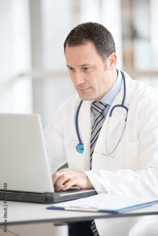 Doctor sitting at his desk with laptop computer Doctor sitting at his desk with laptop computer