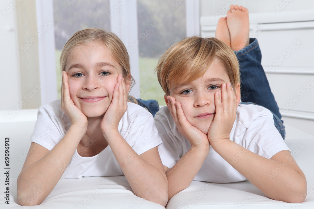 Blond children laying in sofa with hands on chin Blond children laying in sofa with hands on chin