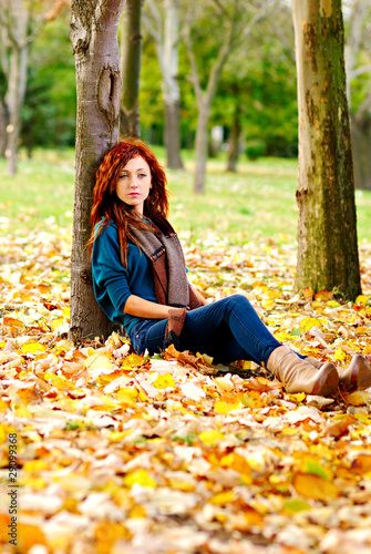Woman is sitting on autumn leaves in a forest