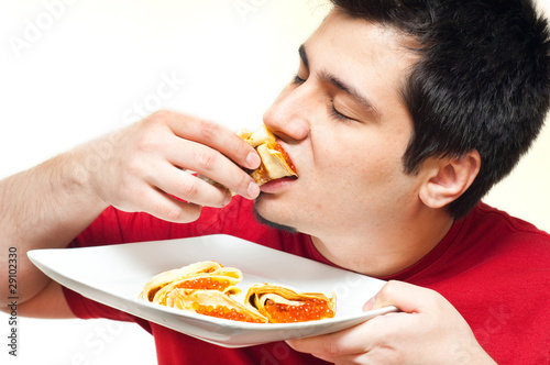 youung man eating pancakes with caviar and sour cream against wh