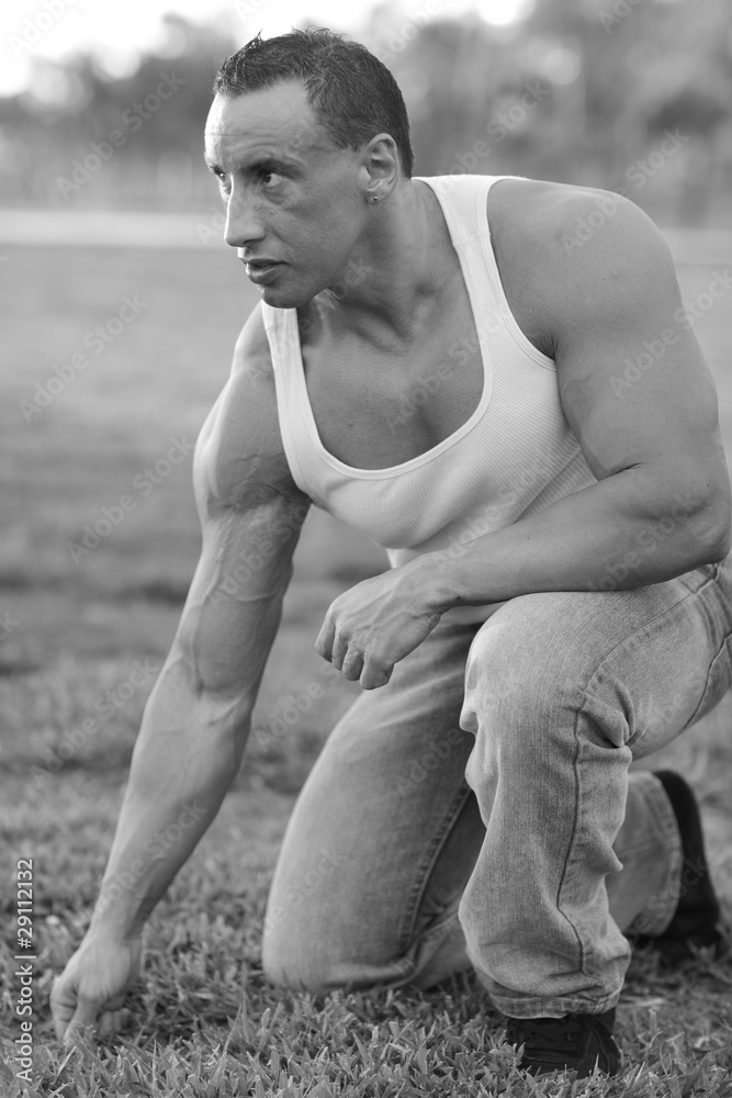Bodybuilder kneeling on the grass