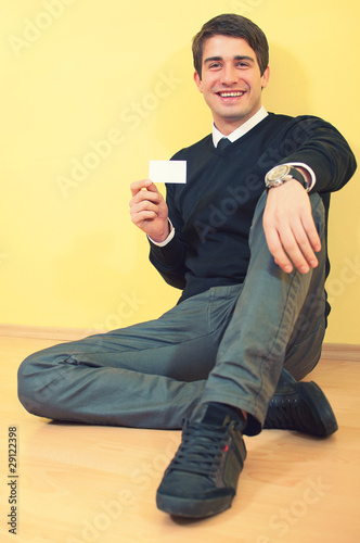 Young sitting smiling handsome business man showing a blank busi
