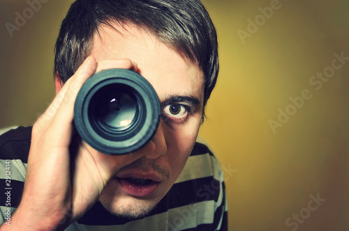 Handsome young man holding camera lens like it was spyglass photo