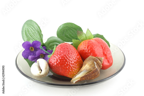 Artificial flowers, strawberries and sea shells on saucer.