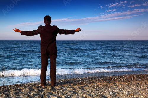 Barefooted man in suit stands back and open hands on stone coast