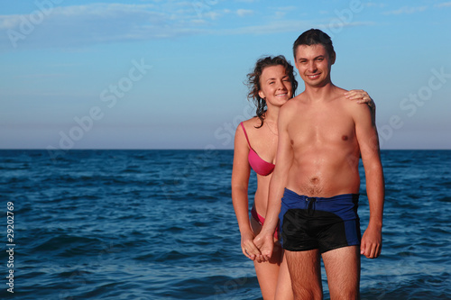 Man and woman in swimsuits stand in water and hold hands