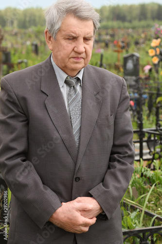 old sad senior in grey suit standing on cemetery