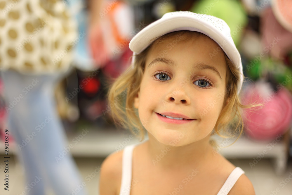 portrait of little girl trying white cap in store and smiling portrait of little girl trying white cap in store and smiling