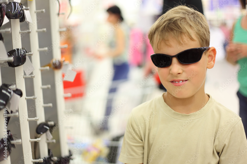 portrait of little boy trying black sunglasses in store portrait of little boy trying black sunglasses in store