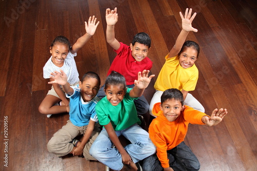 Six school children sitting in classroom hands up