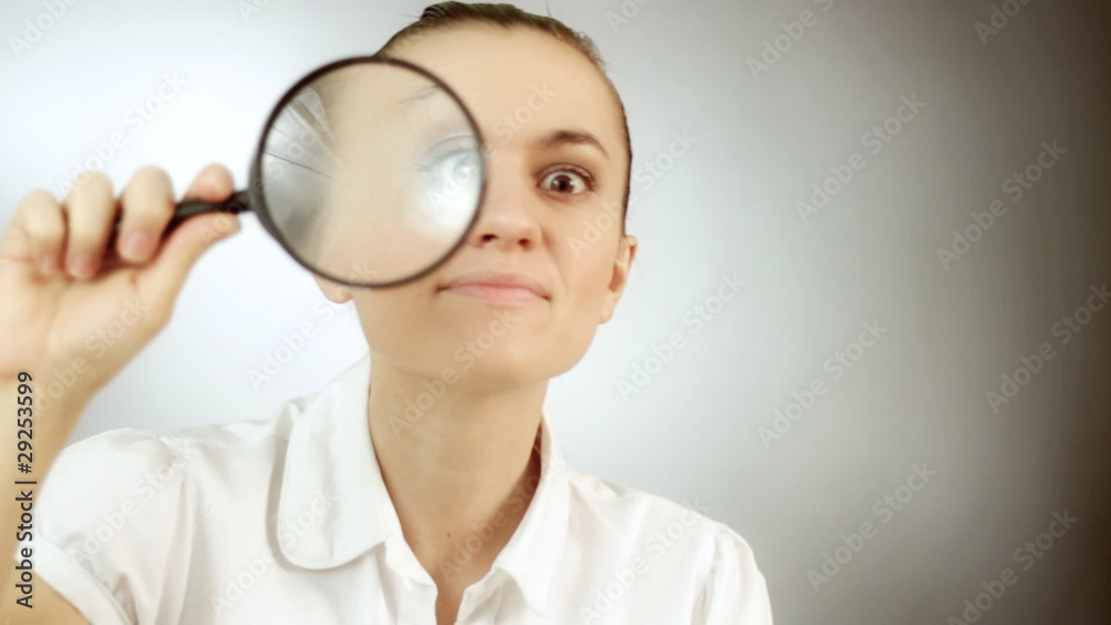 Woman looking through a magnifying glass, grey background Woman looking through a magnifying glass, grey background