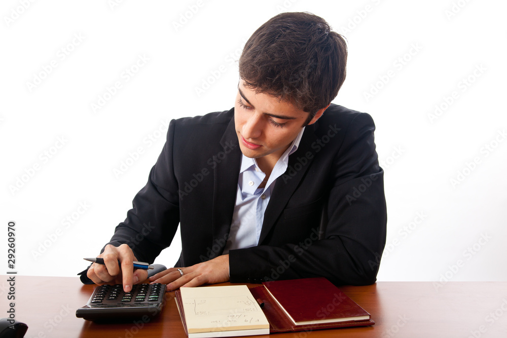 Young businessman using calculator and writing on agenda Young businessman using calculator and writing on agenda