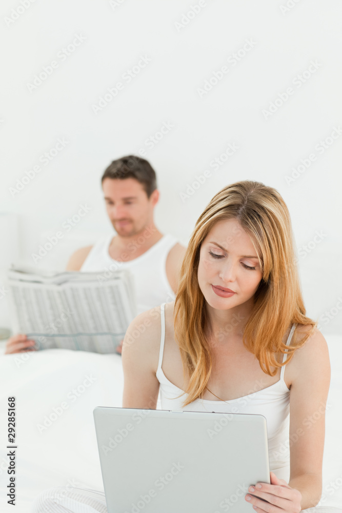Woman is on her laptop while her husband is reading newspaper Woman is on her laptop while her husband is reading newspaper
