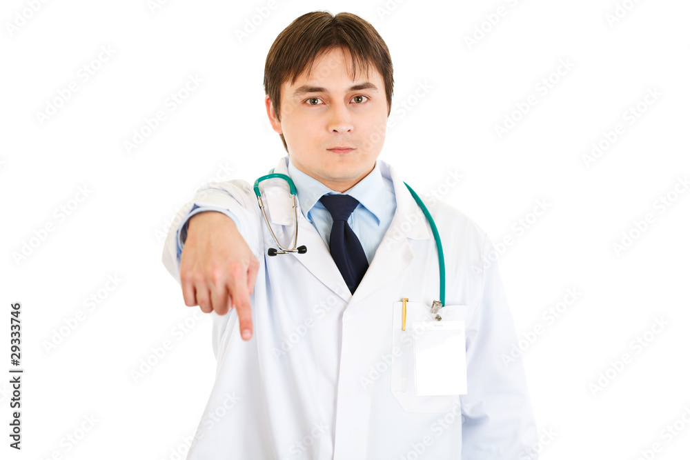 Serious young medical doctor pointing finger down isolated Serious young medical doctor pointing finger down isolated