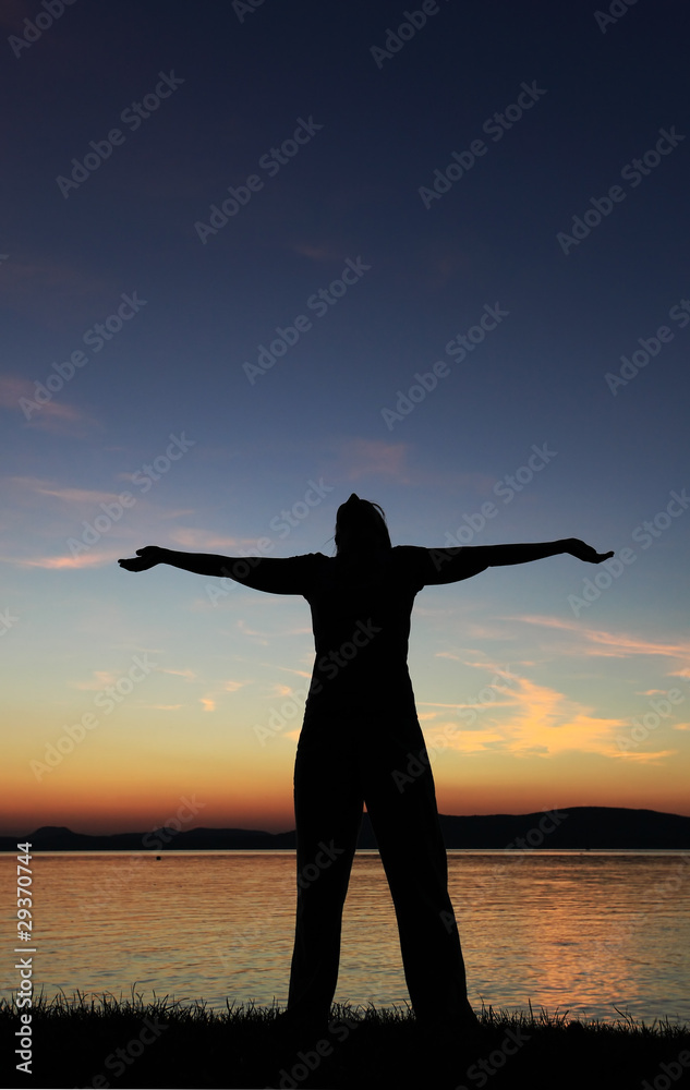 Young woman silhouette raised hands standing at coast