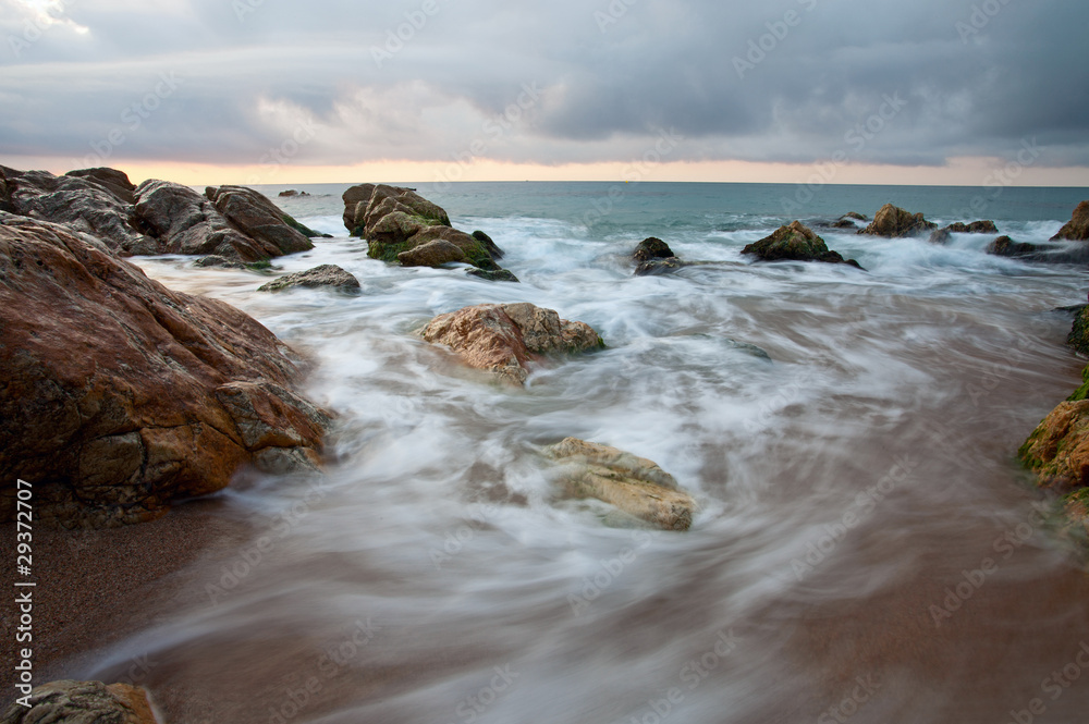 Seascape at sunset with motion blurred waves crashing on rocks
