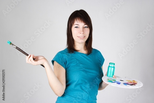 young girl in blue shirt standing and holding brush and palette 