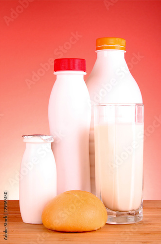 Bottle of milk, loaf and glass on red background