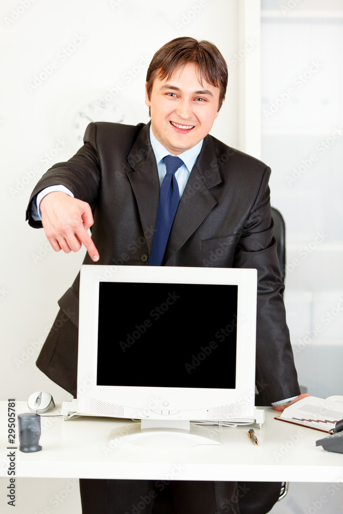 Smiling businessman pointing at monitor with blank screen. Smiling businessman pointing at monitor with blank screen.