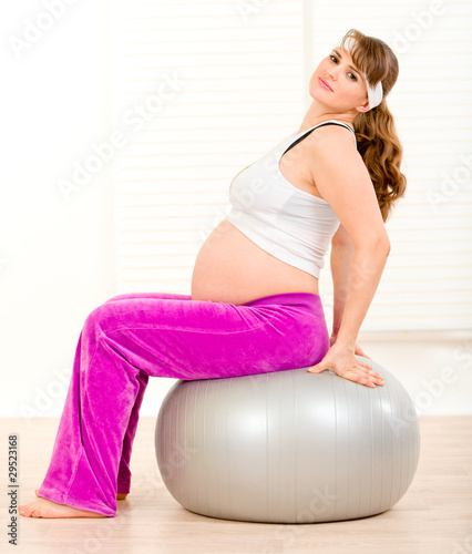 Smiling pregnant woman doing pilates exercises on ball .