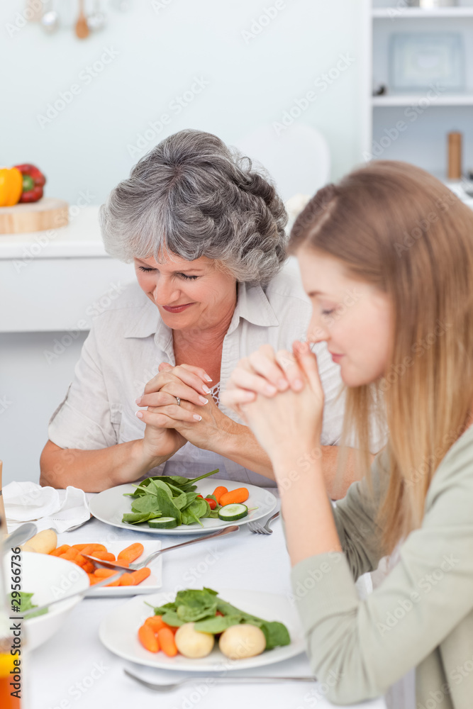 Woman and her mother praying at the table Woman and her mother praying at the table