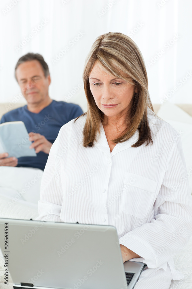 Woman looking at her laptop while her husband is reading Woman looking at her laptop while her husband is reading