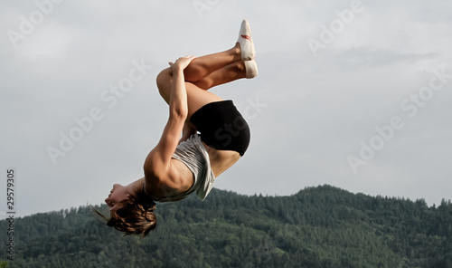 female gymnast doing back somersault in nature