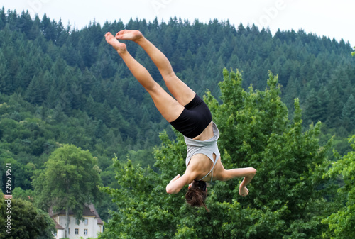 female gymnast doing somersault with spin in front of forest