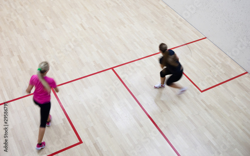 Two female squash players in fast action on a squash court (moti
