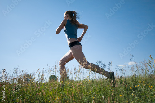 Sport woman running over green grass and sky