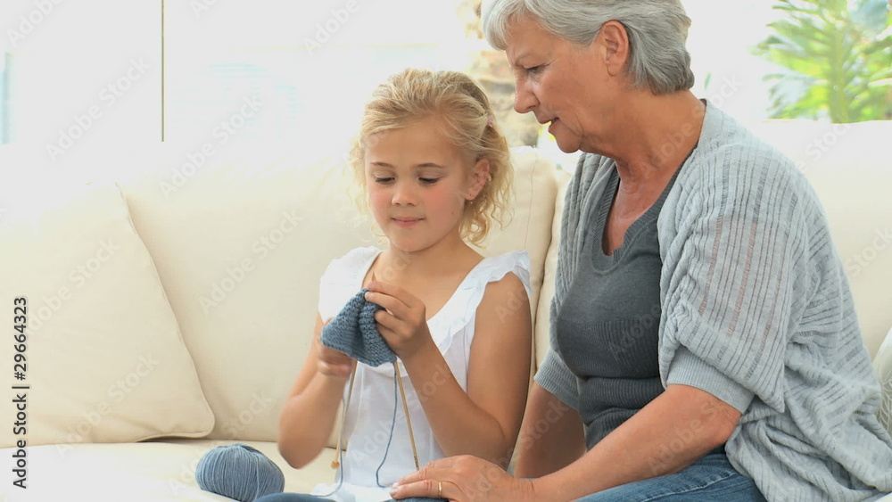 Grandmother teaching her grand daughter how to knit on a sofa Grandmother teaching her grand daughter how to knit on a sofa