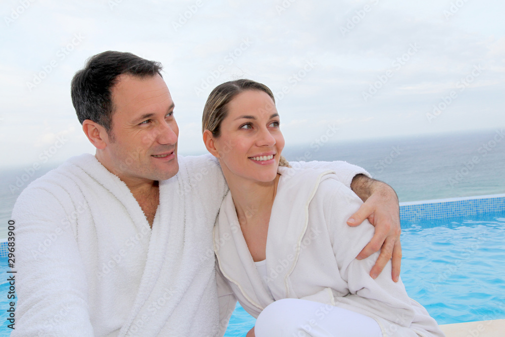 Obraz premium Couple in bathrobe sitting by swimming-pool