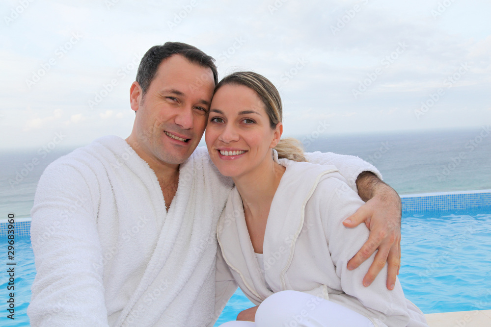 Obraz premium Couple in bathrobe sitting by swimming-pool
