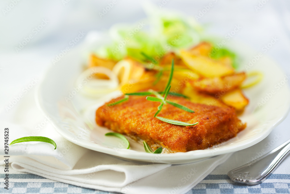 Breaded fish fillet with baked potatoes and herbs