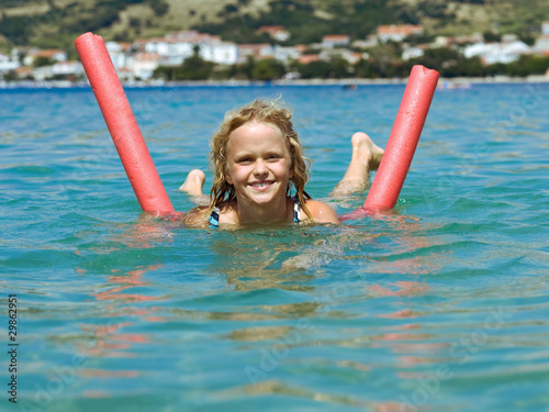 Happy little girl having fan in the sea with swimming aid