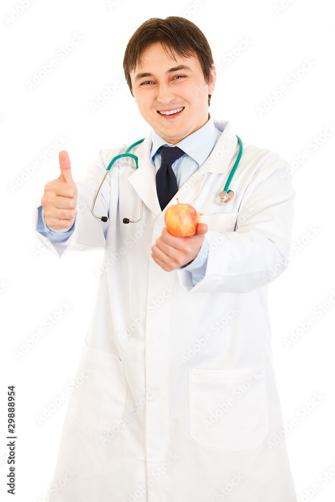 Smiling doctor holding apple and showing thumbs up gesture Smiling doctor holding apple and showing thumbs up gesture
