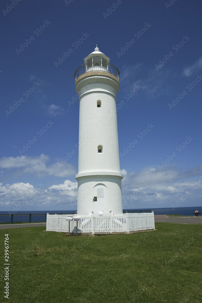 White Lighthouse stands out against green grass and blue sky.