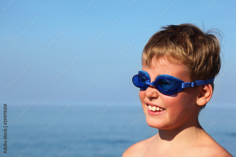Boy in dark blue glasses for swimming stands near sea and smile Boy in dark blue glasses for swimming stands near sea and smile
