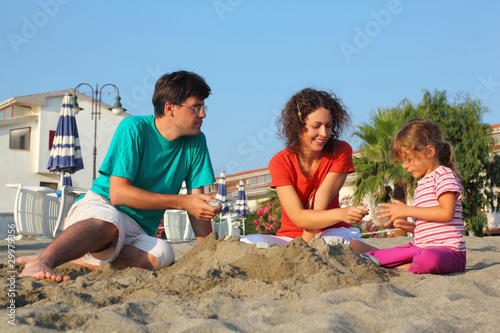 Father with mother and daughter sit on beach in day-time