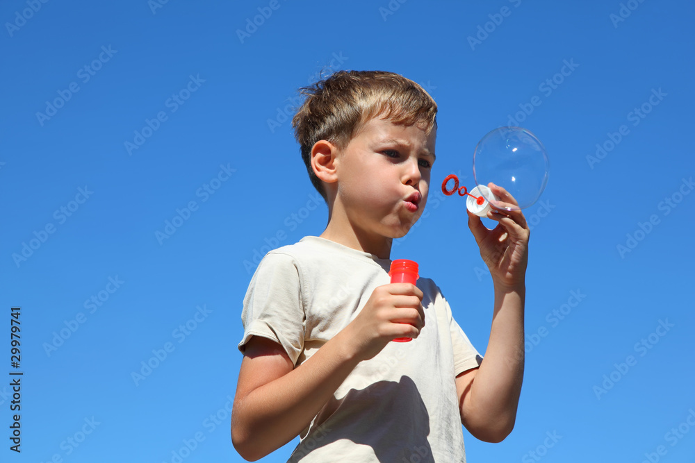 Boy stands straight and inflates soap bubbles in summer Boy stands straight and inflates soap bubbles in summer