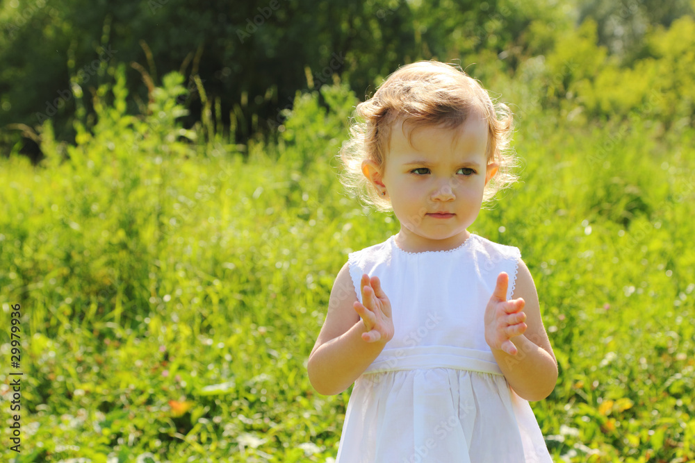 Little girl standing in the grass shows something with her hands Little girl standing in the grass shows something with her hands