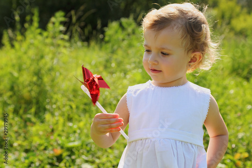 Little girl with the red pinwheel standing in the grass and look