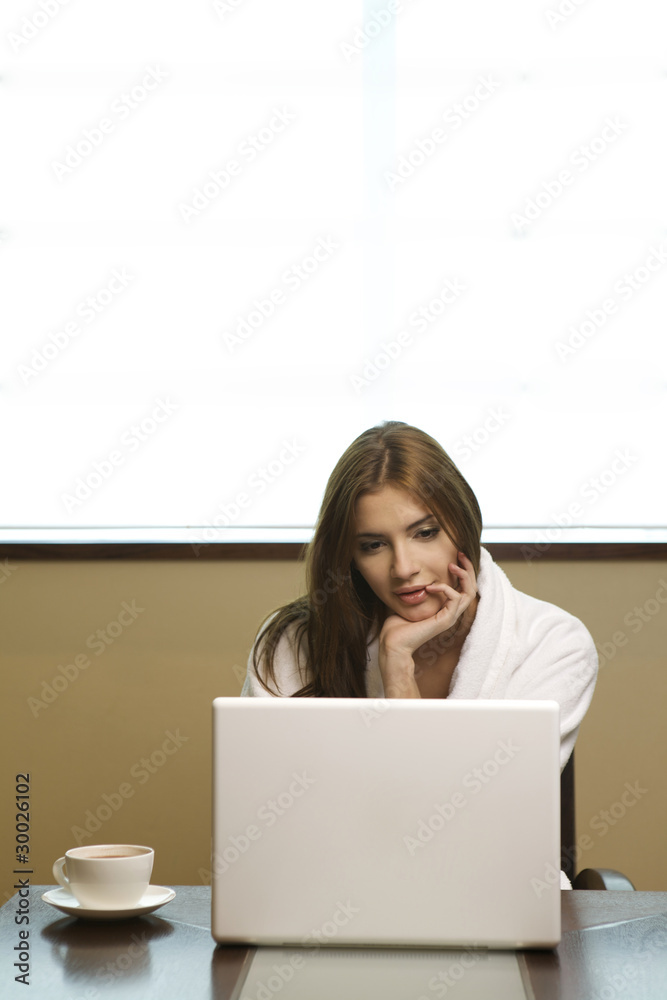 Young woman looks at her laptop computer and drinks her coffee Young woman looks at her laptop computer and drinks her coffee