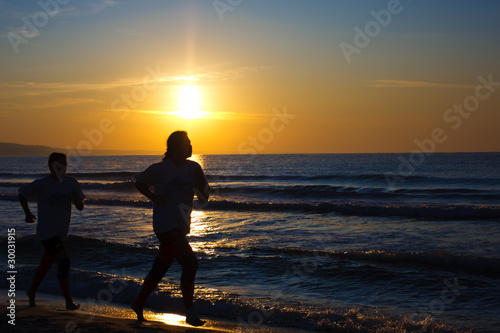 Female and male runners silhouette with a sunset sky and sea
