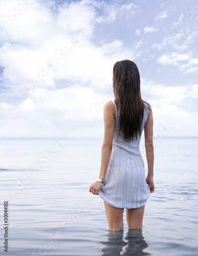 A young woman in a cute dress is standing in the lake water