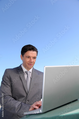 Smiling businessman working outside with laptop computer