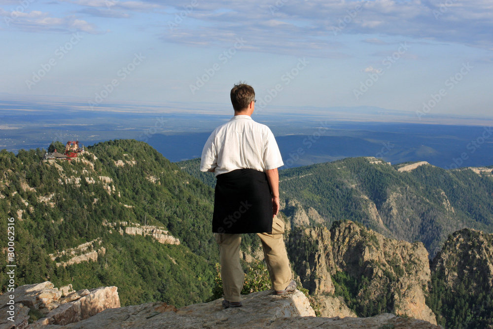 Mann steht auf dem Gipfel und schaut ins Tal