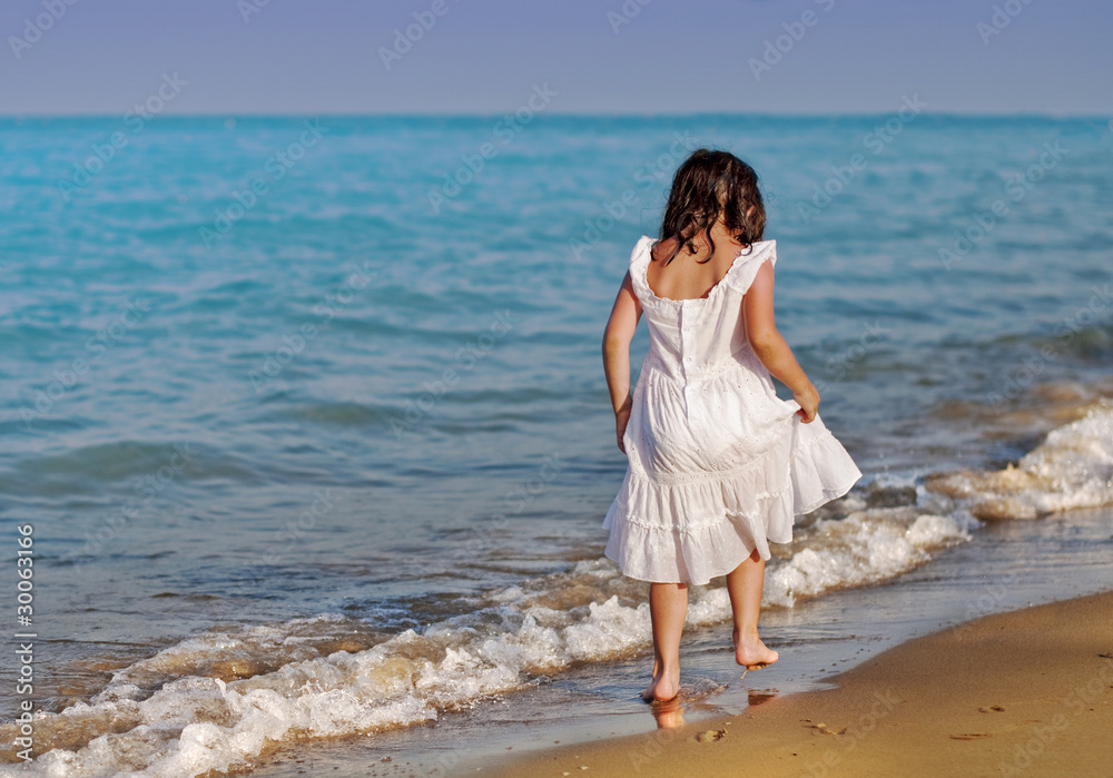 Girl in a white derss walking along a seaside