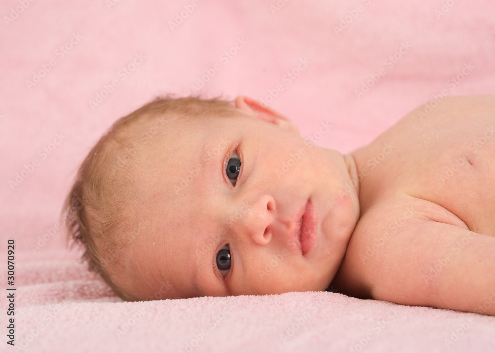 Neugeborenes liegt auf rosa Decke und schaut